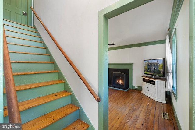 stairway featuring a warm lit fireplace, hardwood / wood-style floors, and visible vents