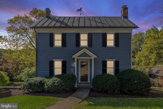 colonial inspired home with a chimney, metal roof, and a standing seam roof
