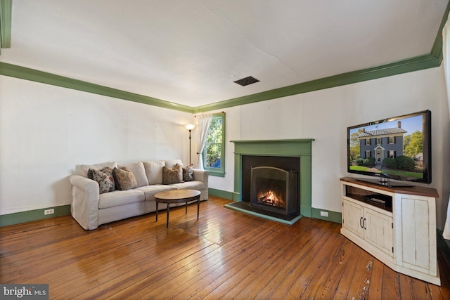 living area featuring baseboards, a warm lit fireplace, ornamental molding, and hardwood / wood-style flooring