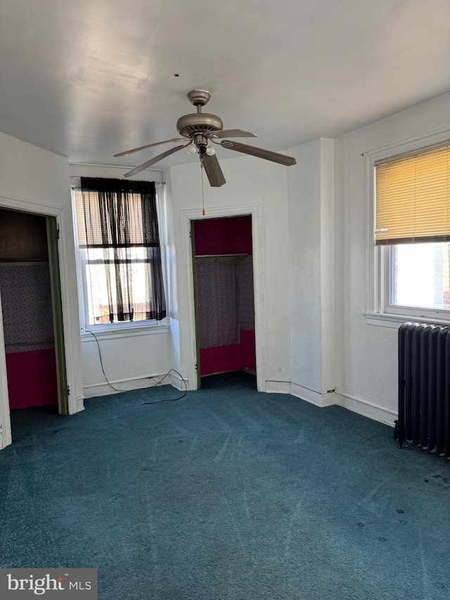 interior space featuring ceiling fan, multiple windows, dark colored carpet, and radiator heating unit