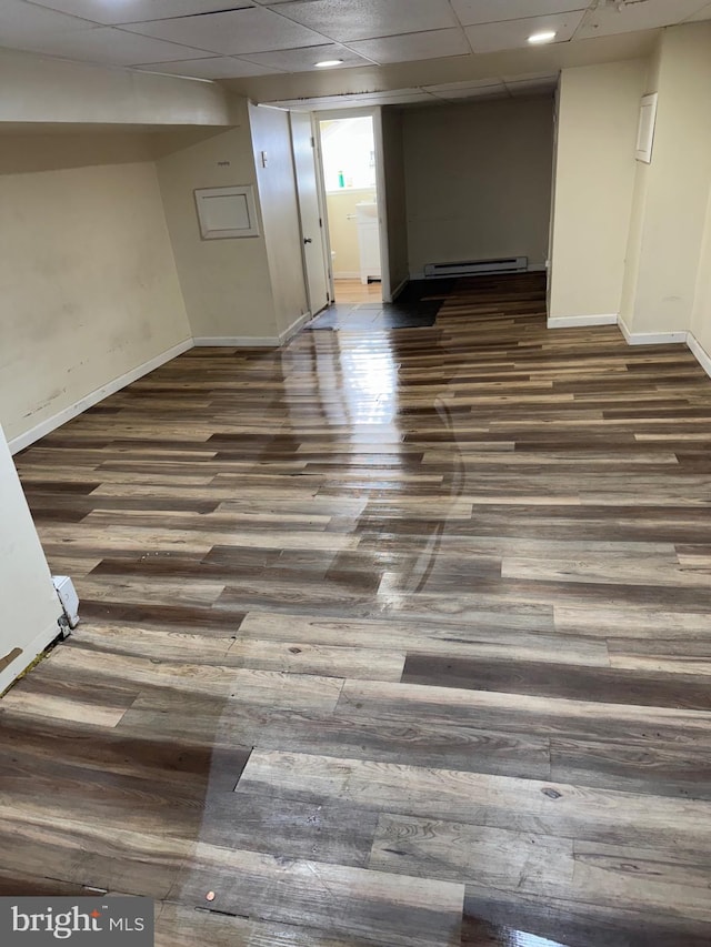 basement with baseboard heating, a paneled ceiling, and dark wood-type flooring