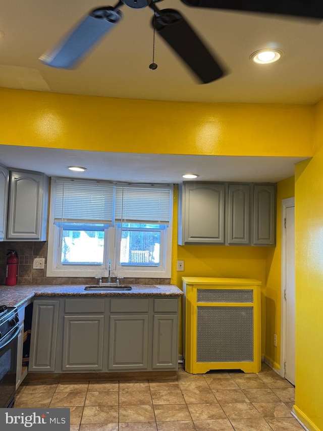 kitchen featuring gray cabinetry, ceiling fan, black stove, sink, and decorative backsplash