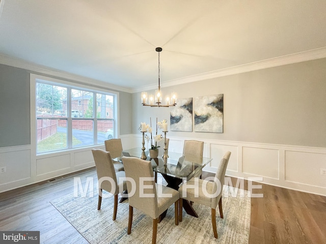 dining room featuring an inviting chandelier, a decorative wall, ornamental molding, and wood finished floors