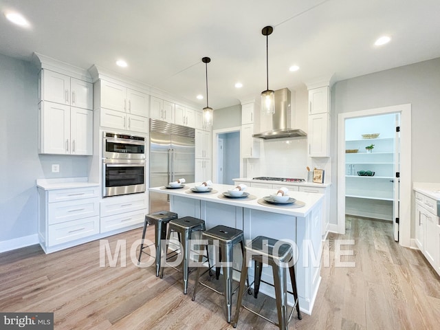 kitchen featuring light wood-style floors, wall chimney exhaust hood, a breakfast bar, appliances with stainless steel finishes, and light countertops