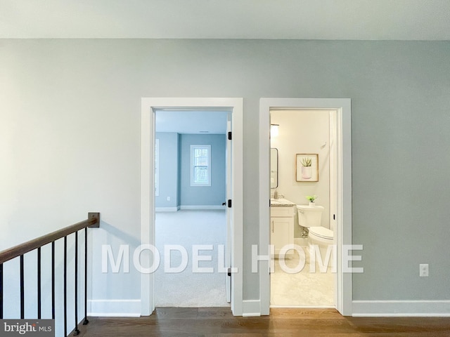 corridor featuring an upstairs landing, dark wood-style flooring, baseboards, and a sink