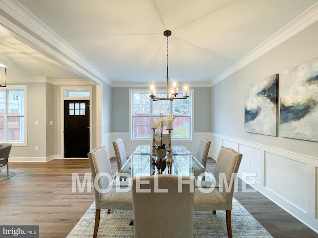 dining area with a decorative wall, a chandelier, crown molding, wainscoting, and wood finished floors
