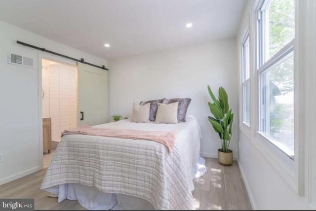 bedroom featuring ensuite bathroom, a barn door, light hardwood / wood-style flooring, and multiple windows