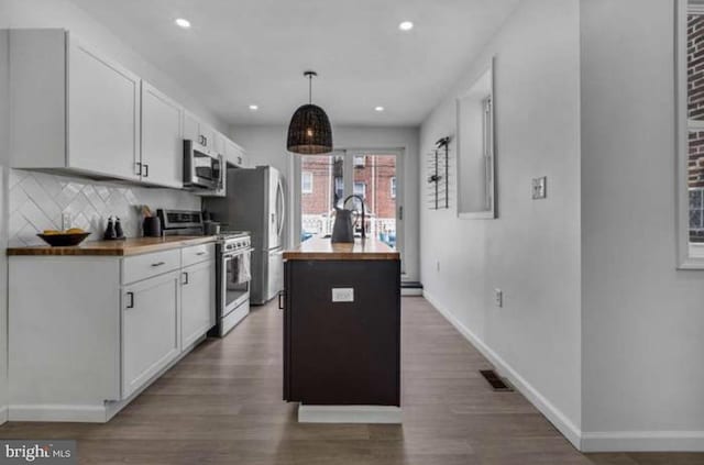 kitchen with appliances with stainless steel finishes, wood counters, white cabinetry, dark wood-type flooring, and a kitchen island with sink