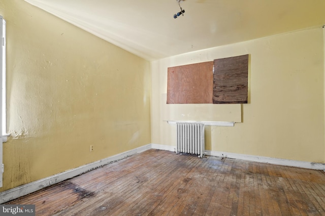 spare room featuring lofted ceiling, radiator heating unit, and wood-type flooring