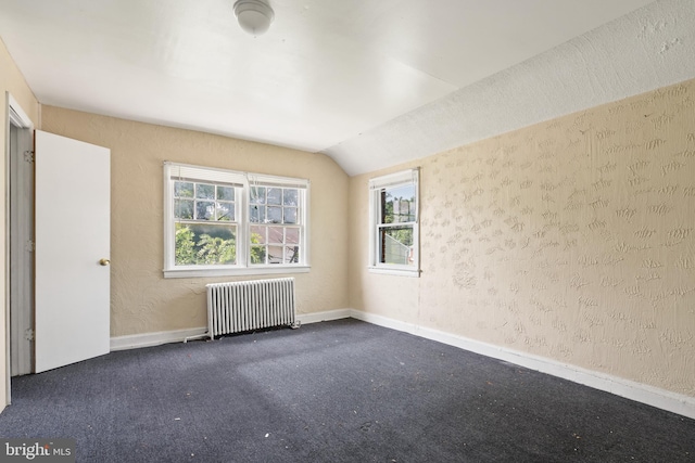 spare room featuring dark colored carpet, vaulted ceiling, and radiator heating unit