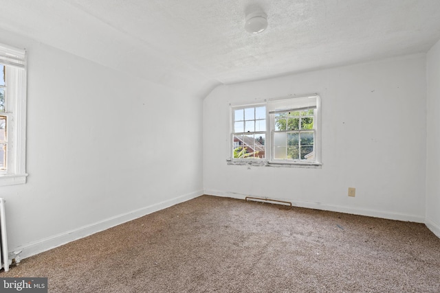 unfurnished room with carpet flooring, a textured ceiling, vaulted ceiling, and radiator heating unit