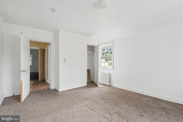 unfurnished bedroom featuring carpet floors, a textured ceiling, a closet, and radiator heating unit