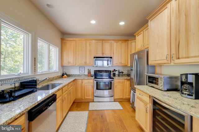 kitchen with light stone counters, wine cooler, sink, light hardwood / wood-style flooring, and stainless steel appliances