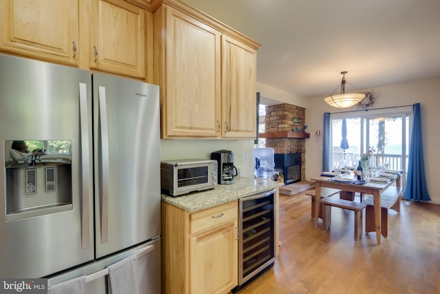 kitchen featuring light wood-type flooring, a stone fireplace, pendant lighting, wine cooler, and stainless steel refrigerator with ice dispenser