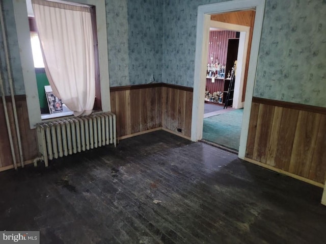 spare room featuring dark wood-type flooring, wood walls, and radiator heating unit