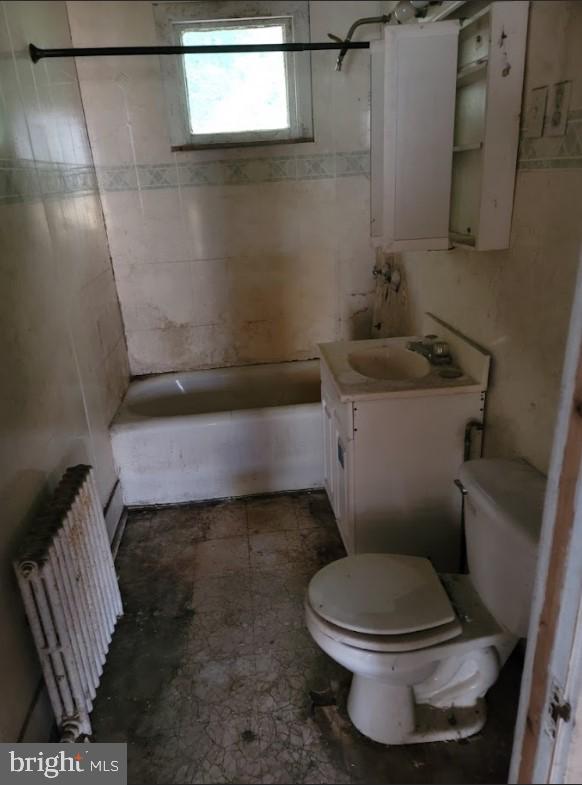 full bathroom with toilet, tiled shower / bath combo, vanity, and radiator