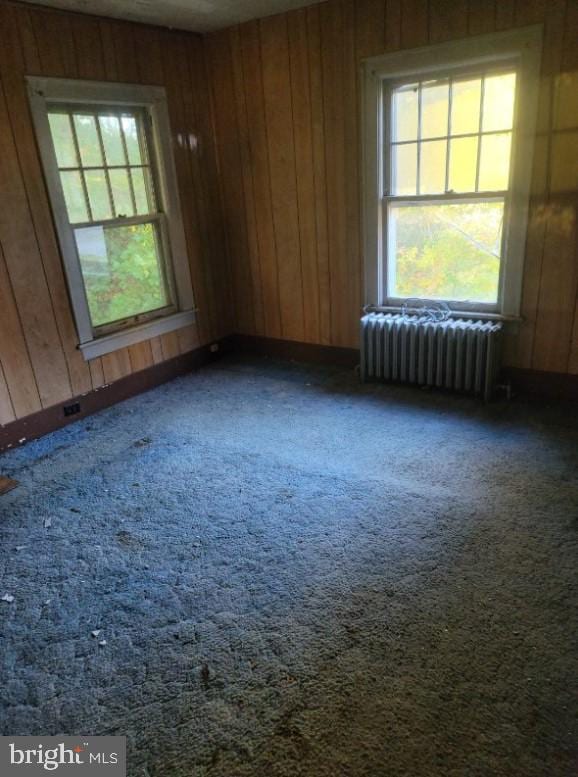 carpeted spare room with a wealth of natural light, radiator heating unit, and wood walls