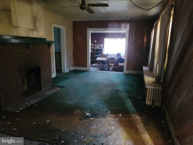 unfurnished living room featuring ceiling fan, wood walls, and a fireplace