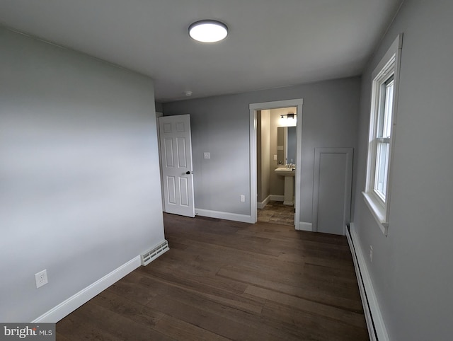 unfurnished bedroom with a baseboard radiator, dark wood-type flooring, multiple windows, and ensuite bathroom