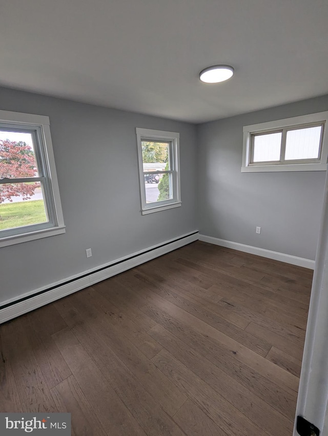 empty room with dark hardwood / wood-style floors, a healthy amount of sunlight, and baseboard heating