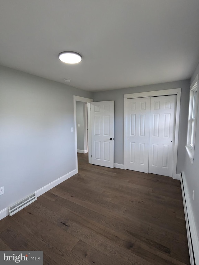 unfurnished bedroom with a baseboard heating unit, dark hardwood / wood-style floors, and a closet