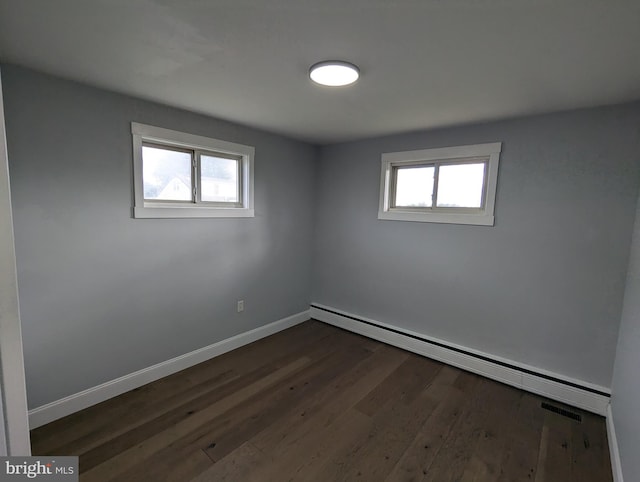 spare room with a healthy amount of sunlight, a baseboard radiator, and dark hardwood / wood-style flooring