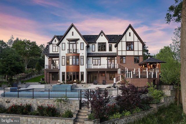 back house at dusk featuring a patio, a fenced in pool, and a balcony