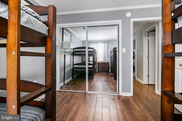 unfurnished bedroom with a closet, stacked washing maching and dryer, crown molding, a textured ceiling, and dark hardwood / wood-style flooring