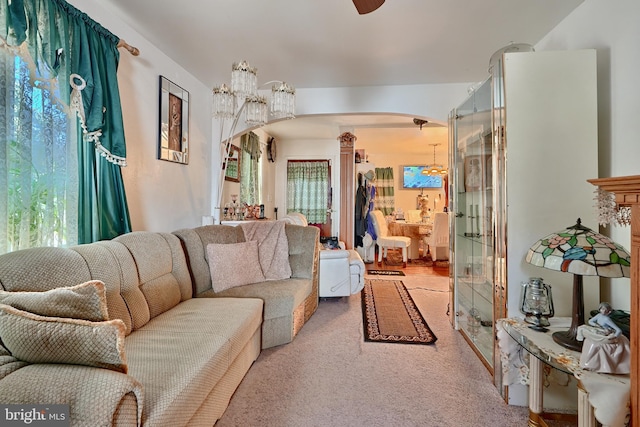 carpeted living area with arched walkways, ceiling fan with notable chandelier, and decorative columns