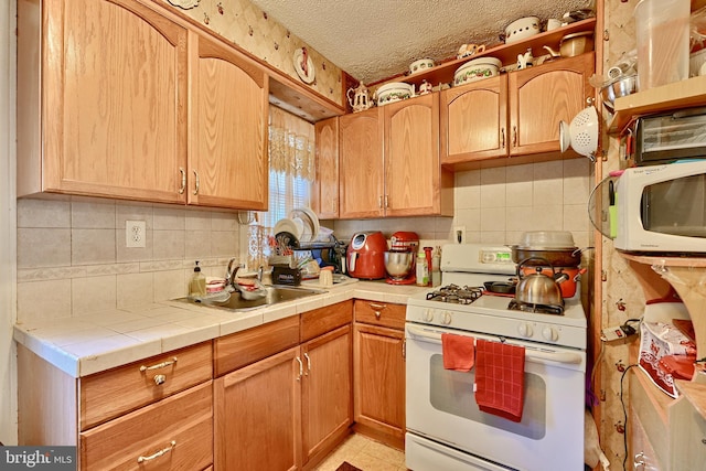 kitchen featuring tile counters, sink, light tile patterned floors, a textured ceiling, and white appliances