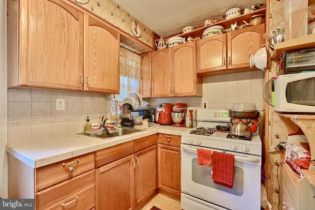 kitchen featuring a sink, a textured ceiling, tasteful backsplash, white appliances, and tile counters