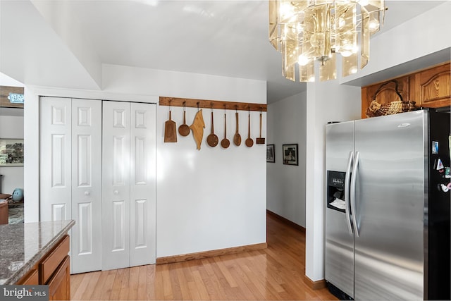 kitchen with stainless steel refrigerator with ice dispenser, a chandelier, stone counters, and light wood-type flooring