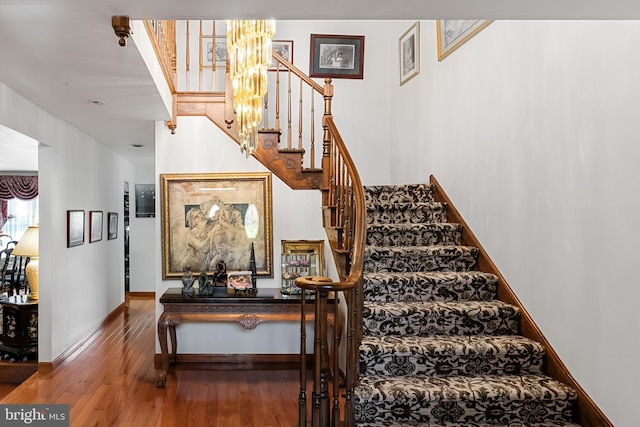 stairway with an inviting chandelier and wood-type flooring