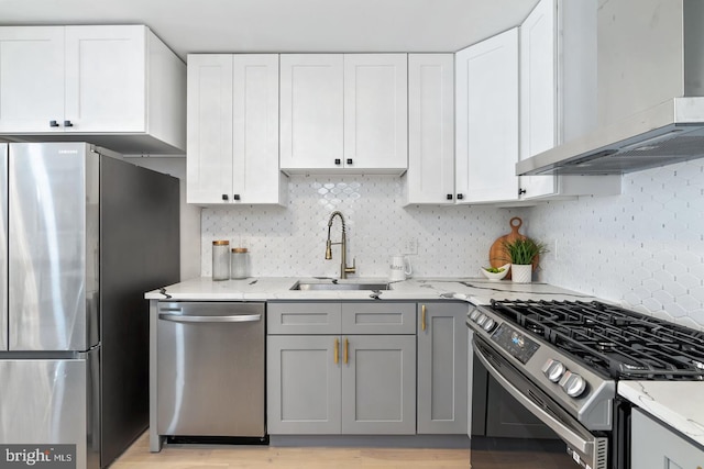 kitchen with stainless steel appliances, wall chimney range hood, sink, and white cabinets