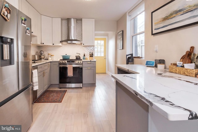 kitchen with light stone countertops, light hardwood / wood-style flooring, gray cabinets, wall chimney exhaust hood, and stainless steel appliances