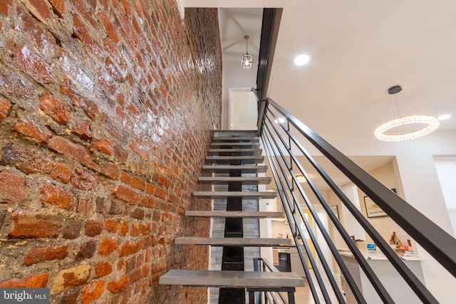 stairway featuring a notable chandelier and brick wall