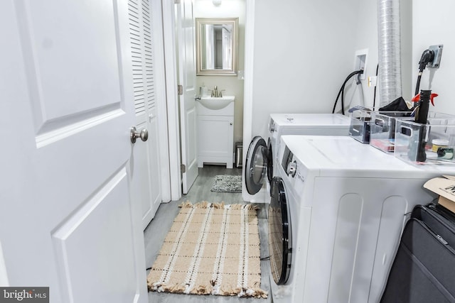 clothes washing area featuring sink, washing machine and clothes dryer, and hardwood / wood-style floors