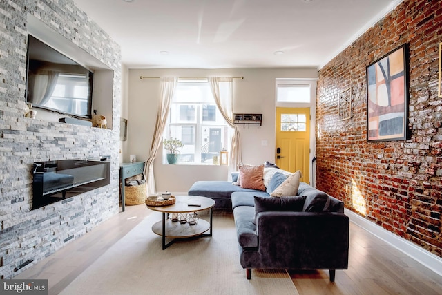 living room featuring brick wall, wood-type flooring, a fireplace, and a wealth of natural light