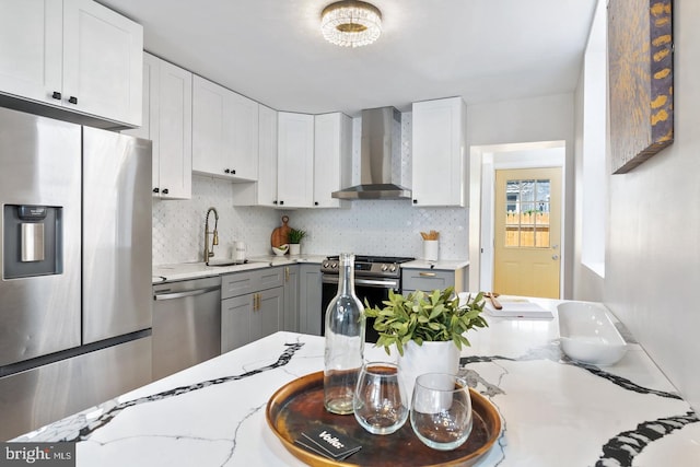 kitchen with wall chimney range hood, white cabinets, stainless steel appliances, and backsplash