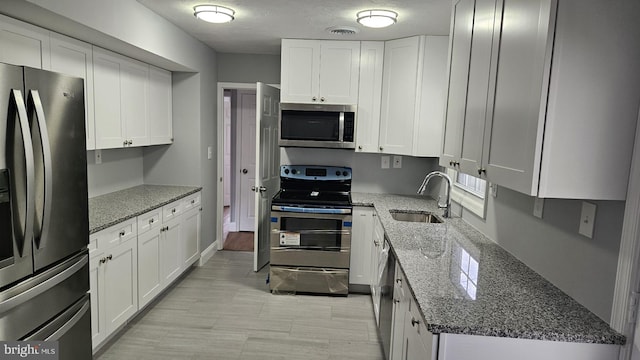 kitchen with dark stone counters, sink, white cabinetry, appliances with stainless steel finishes, and a textured ceiling