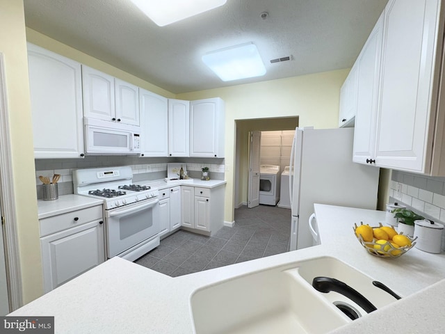 kitchen with sink, white appliances, washer and clothes dryer, decorative backsplash, and white cabinets