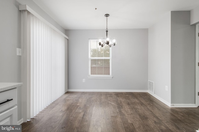 unfurnished dining area featuring dark wood finished floors, an inviting chandelier, visible vents, and baseboards