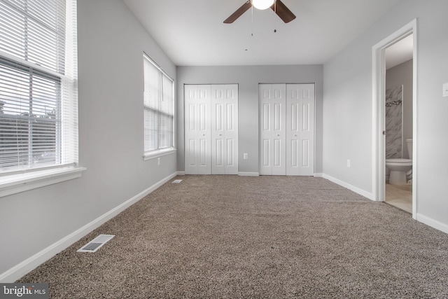 unfurnished bedroom featuring ensuite bathroom, carpet floors, multiple closets, and ceiling fan