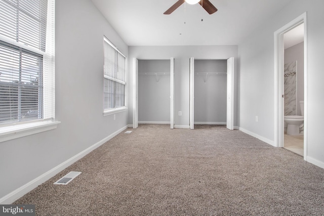 unfurnished bedroom featuring multiple closets, carpet flooring, ensuite bath, and ceiling fan