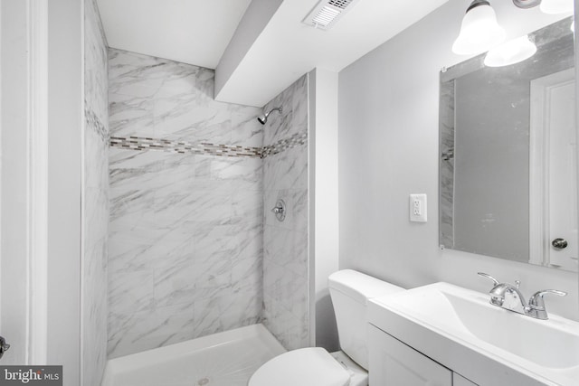 bathroom with a tile shower, toilet, and vanity