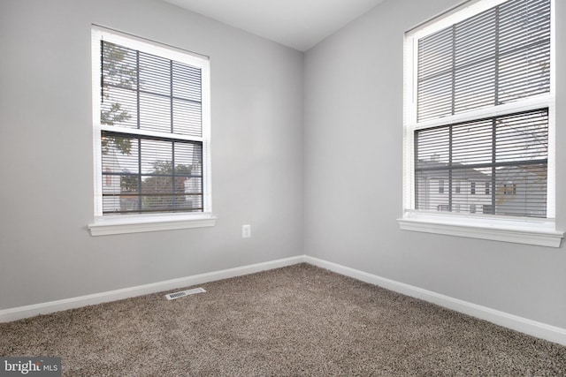 carpeted spare room featuring baseboards, visible vents, and plenty of natural light