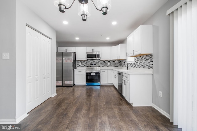 kitchen with appliances with stainless steel finishes, backsplash, white cabinetry, dark wood-type flooring, and a notable chandelier