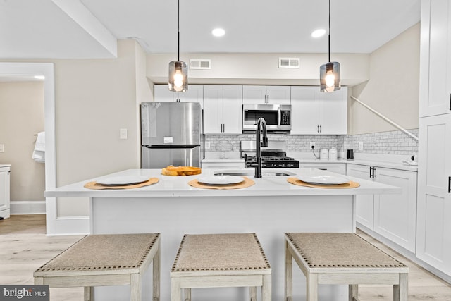 kitchen with a breakfast bar area, stainless steel appliances, a center island with sink, and pendant lighting