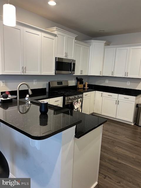 kitchen with dark hardwood / wood-style flooring, white cabinetry, stainless steel appliances, pendant lighting, and dark stone countertops