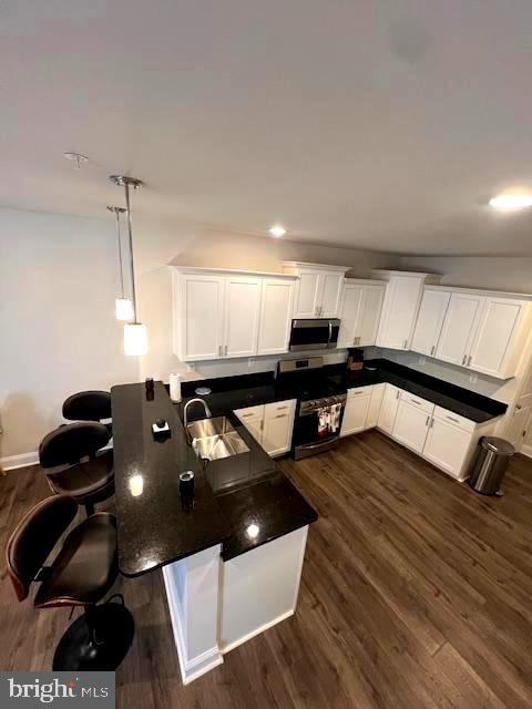 kitchen featuring appliances with stainless steel finishes, sink, decorative light fixtures, white cabinets, and dark wood-type flooring